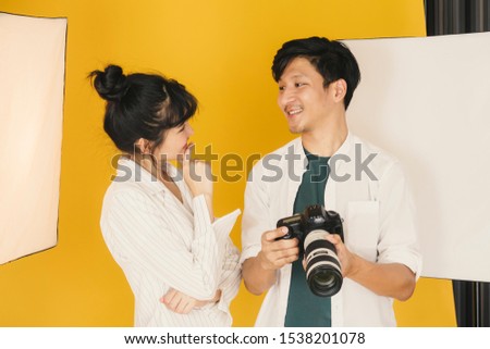 Happy Beautiful Asian young model and Young male professional photographer smile after checking pictures on the camera in the studio.