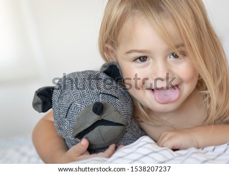 Closeup portrait of a cute baby boy making faces, showing the tongue, having fun at home with his soft toy, happy healthy carefree childhood