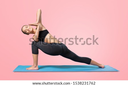 Active lady doing workout for legs on purple fitness mat. Female athlete in pink headband and orange sweatshirt posing on isolated background
    
    - Image