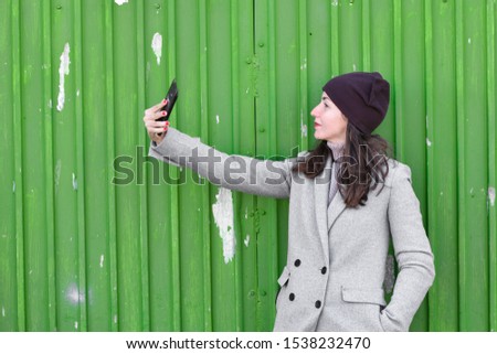 girl takes a selfie on a green background. wearing a hat and coat. place for writing. dressed in a cold pagoda. clothes and style. natural emotions