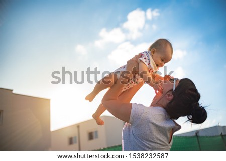An emotional picture of 1 year old baby and her mother holding her up in the air against blue sky and bright sun