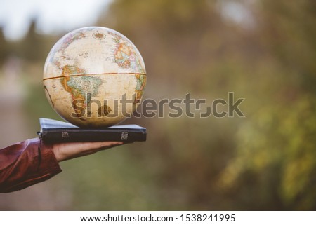 A closeup shot of a person holding bible with desk globe on top with a blurred background