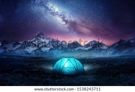 Camping in the mountains under the stars. A tent pitched up and glowing under the milky way. Photo composite. Royalty-Free Stock Photo #1538243711