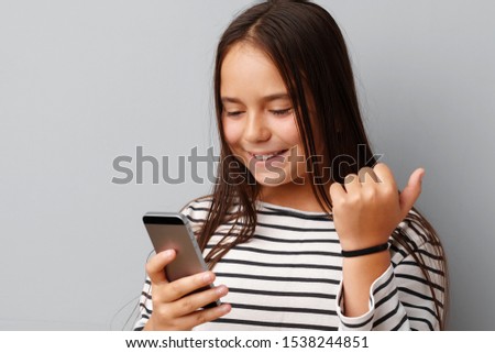 Happy casual little girl looking at her phone over gray background