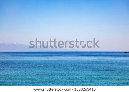 Blue shades horizon. Clear blue sky and rippled sea, blur mountains with snow background, Greece, Aegean sea in spring