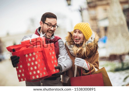 Young couple dressed in winter clothing holding gift boxes outdoor. 