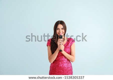 Beautiful young female singer with microphone on light background
