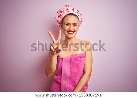 Young beautiful woman wearing towel and bath hat after shower over pink isolated background showing and pointing up with fingers number two while smiling confident and happy.