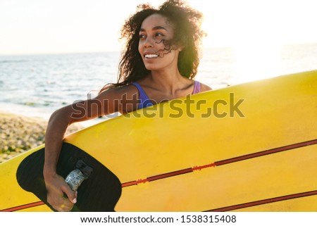 Image of beautiful african american woman in swimsuit holding surfboard and smiling on summer beach