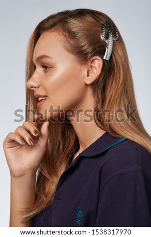  Profile portrait shot of a smiling lady with blond hair, posing on a blue background. She has a silver hair clip in the form of cactus. The girl is wearing a dark blue T-shirt Royalty-Free Stock Photo #1538317970
