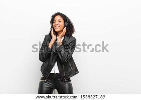 young pretty black woman listening music with a headphones wearing a leather jacket against white wall
