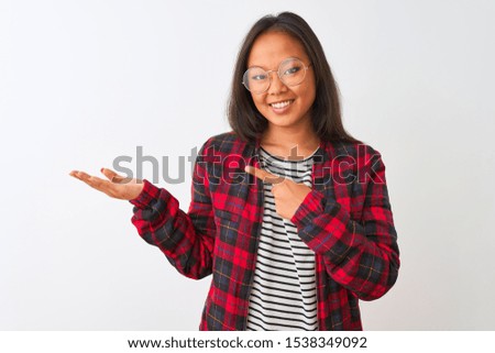 Young chinese woman wearing t-shirt jacket and glasses over isolated white background amazed and smiling to the camera while presenting with hand and pointing with finger.