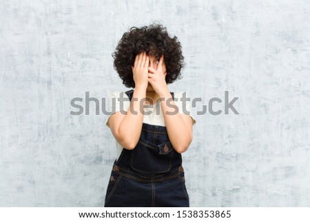 young pretty afro woman covering face with hands, peeking between fingers with surprised expression and looking to the side