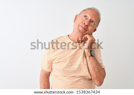 Senior grey-haired man wearing striped t-shirt standing over isolated white background with hand on chin thinking about question, pensive expression. Smiling with thoughtful face. Doubt concept.