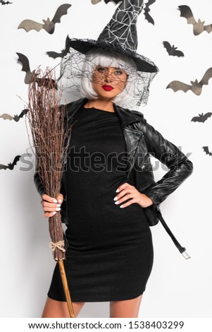 attractive woman in witch hat and wig holding broom in Halloween