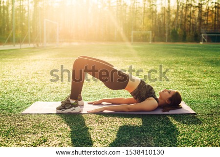 Healthy sports lifestyle. Young woman doing yoga in stadium. Bridge pose.