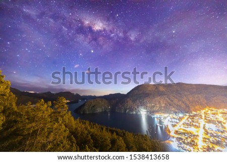 San Martin de los Andes town nightscape view. The Milky Way as seen from the southern hemisphere during twilight on an awesome natural scenery with the Lacar lake blue waters and the illuminated town