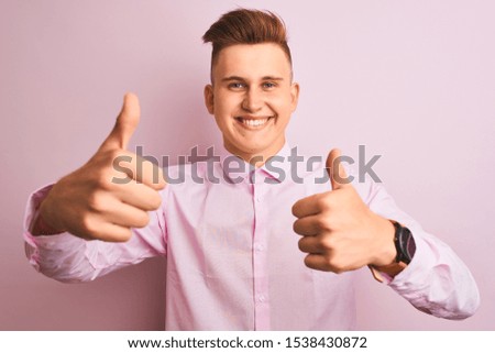 Young handsome businessman wearing elegant shirt standing over isolated pink background approving doing positive gesture with hand, thumbs up smiling and happy for success. Winner gesture.