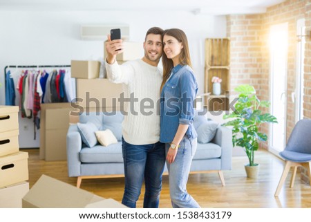 Beautiful couple taking a selfie photo using smartphone at new apartment, smiling happy for new house