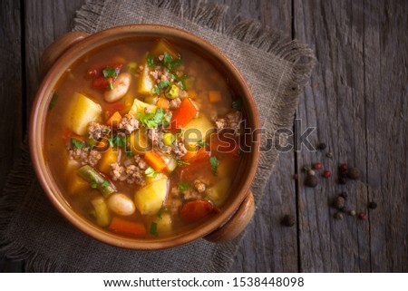 Hamburger soup made with fresh vegetables and ground meat on dark wooden background