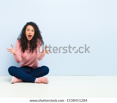 young pretty woman feeling happy, astonished, lucky and surprised, like saying omg seriously? Unbelievable sitting on floor