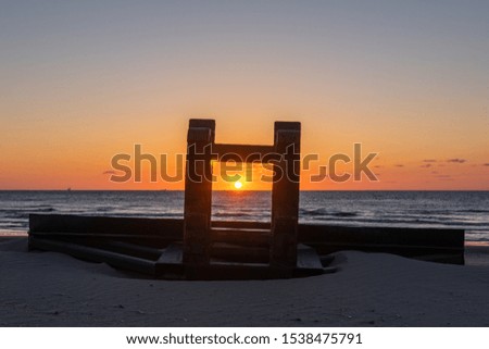 Silhouete of metal construction design like stool on the sea beach in beautiful sunset with serene sea in the background