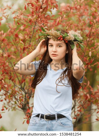 Beautiful pensive teenage girl in the autumn wreath of leaves and berries on a background of red leaves