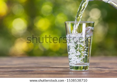 water from jug pouring into glass on wooden table outdoors Royalty-Free Stock Photo #1538538710