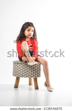 Little Indian girl wearing shoes while sitting on small stool, isolated over white background