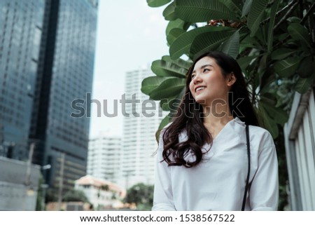 Smiling cute girl on white shirt walking on the city street looking at skyscraper.