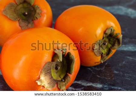 Close-up of three orange kakis on dark marble in horizontal