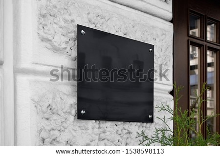 Blank black glass signplate on textured wall mockup. Empty lawyer square nameplate mock up. Clear glassy banner for shop or office entry mokcup template.
