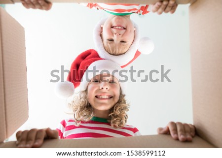 Happy children looking into the box. Funny surprised kids unpack Christmas gift box. Xmas holiday concept. Low angle view. 