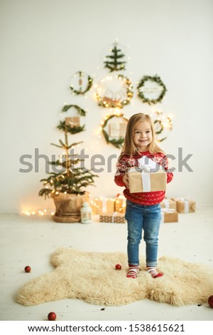 portrait of a beautiful little girl in a red Christmas sweater with reindeer on a white peel with a lantern and gifts