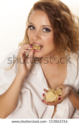 beautiful girl in a white shirt eats potato chips