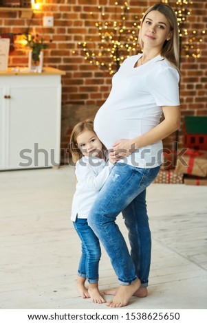 A portrait of a little daughter with her pregnant mother in the kitchen on a brick background with a blurred lights