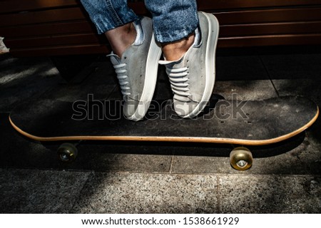 Staying at skateboard on concrete walkway. Jeans pants, white sport shoe.