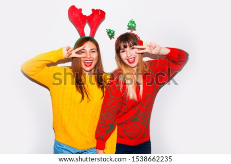  Two cute young woman in santa claus hat emotionally posing on new year photoshoot. Joyful and happy young females.Smiling having fun, ready for celebration. Bright holiday image of best friends.