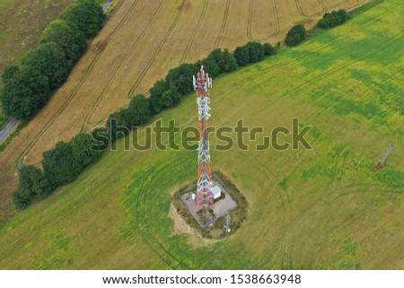 Aerial drone perspective view on high telecommunication steel tower placed in rural area surrounded by meadows, forest and wheat fields.