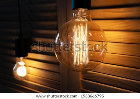 Decorative incandescent lamp hangs near a wooden lattice and shines at night.