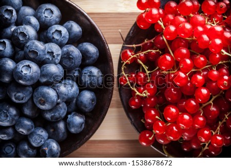 Berries fresh overhead vibrant arrangement of blueberries and red currant in black plates close up on rustic wooden table on bright light studio shot