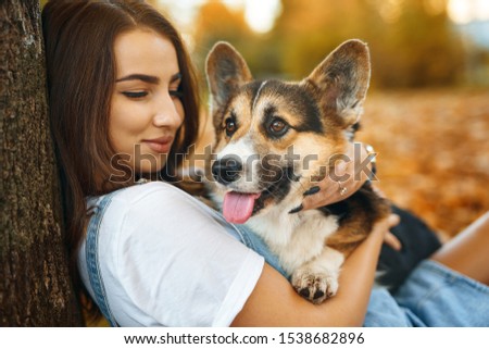smiling happy woman together with Welsh Corgi Pembroke dog in a park outdoors. Young female owner huging pet in park at fall on the orange foliage background. Focus on the dog. Concept friendship with