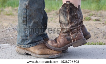 Country girl standing with tiptoes on cowboy’s boots.  Short girl problems. Royalty-Free Stock Photo #1538706608