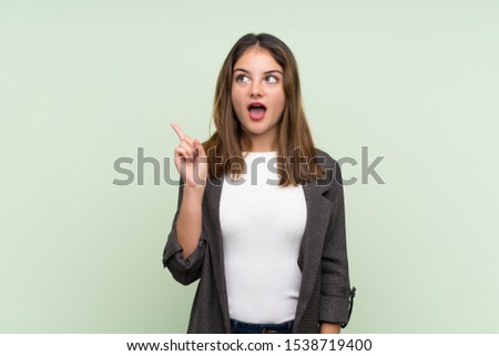 Young brunette girl with blazer over isolated green background thinking an idea pointing the finger up