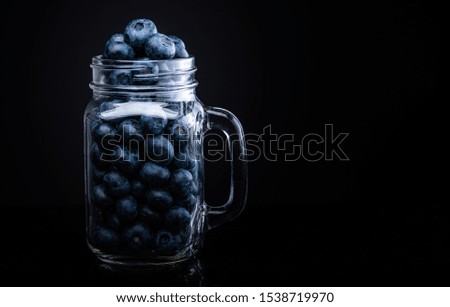 Blueberries in glass jar isolated on black background.