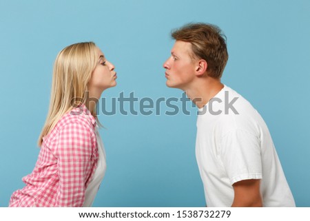 Young pretty couple two friends guy girl in white pink empty blank design t-shirts posing isolated on pastel blue background studio portrait. People lifestyle concept. Mock up copy space. Kissing