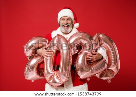 Laughing elderly gray-haired mustache bearded Santa man in Christmas hat posing isolated on red background. New Year 2020 celebration concept. Mock up copy space. Hold colorful numeral air balloons
