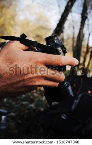 Man's hands holding black camera on autumn forest background