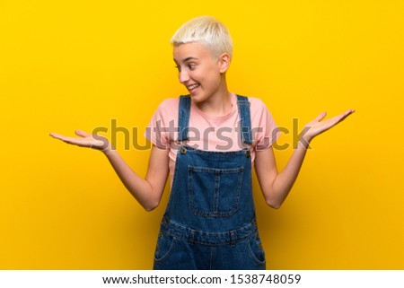 Teenager girl with overalls on yellow background holding copyspace with two hands