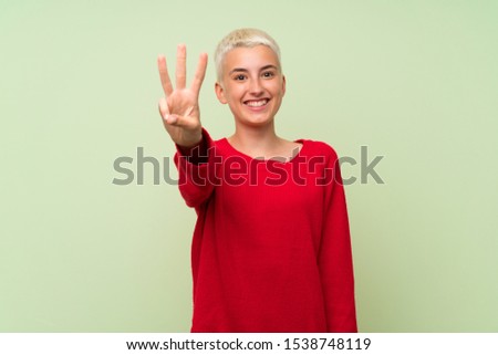 Teenager girl with white short hair over green wall happy and counting three with fingers